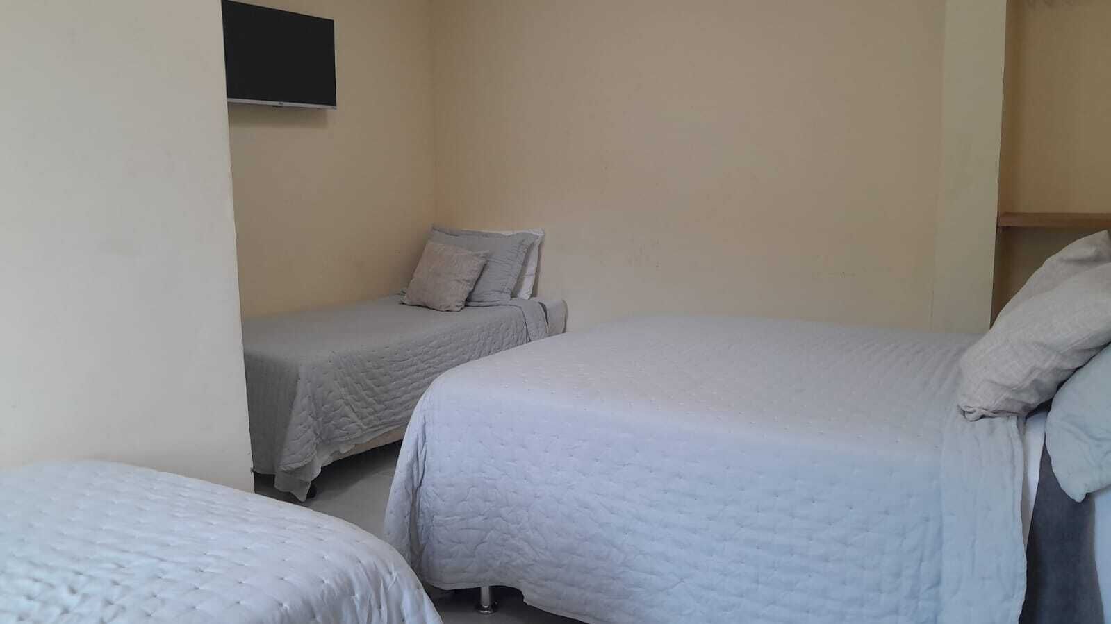 Een kamer met twee bedden, elk voorzien van een grijs geborduurde sprei en kussens. Een flatscreen televisie is aan de muur boven het linkerbed bevestigd.