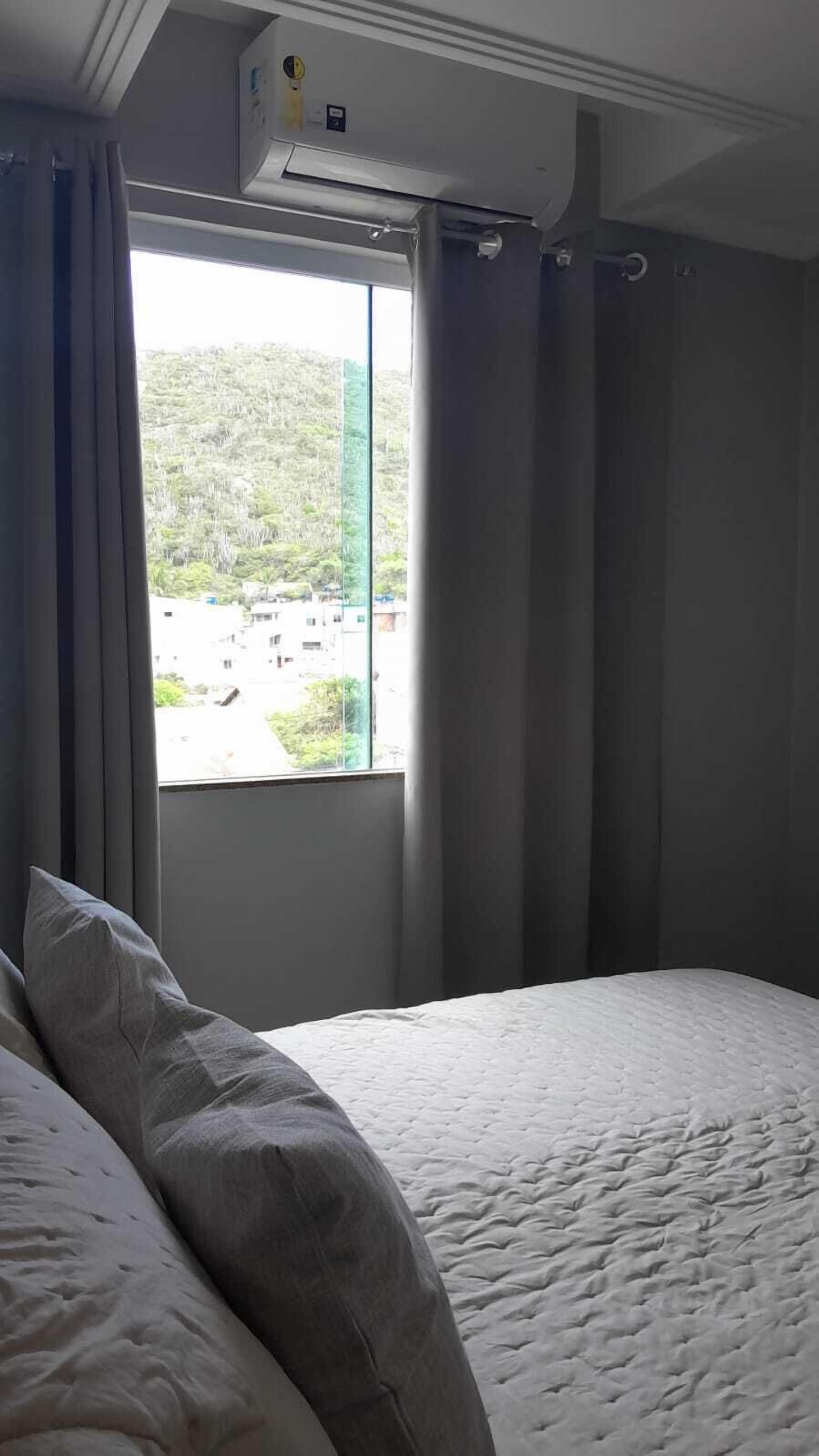 Una camera d'albergo con un letto, una finestra con tende e un condizionatore d'aria.