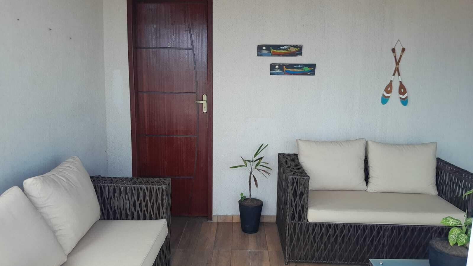 A room with a wooden door, wicker furniture, a potted plant, and wall decorations including a boat and paddles.