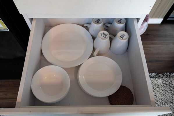 Un cajón con platos, tazones y una taza de café blancos.