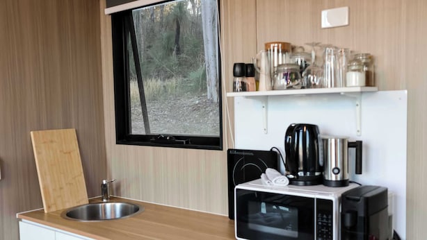 Una kitchenette compacta con un lavamanos, un microondas, una tetera y una cafetera.