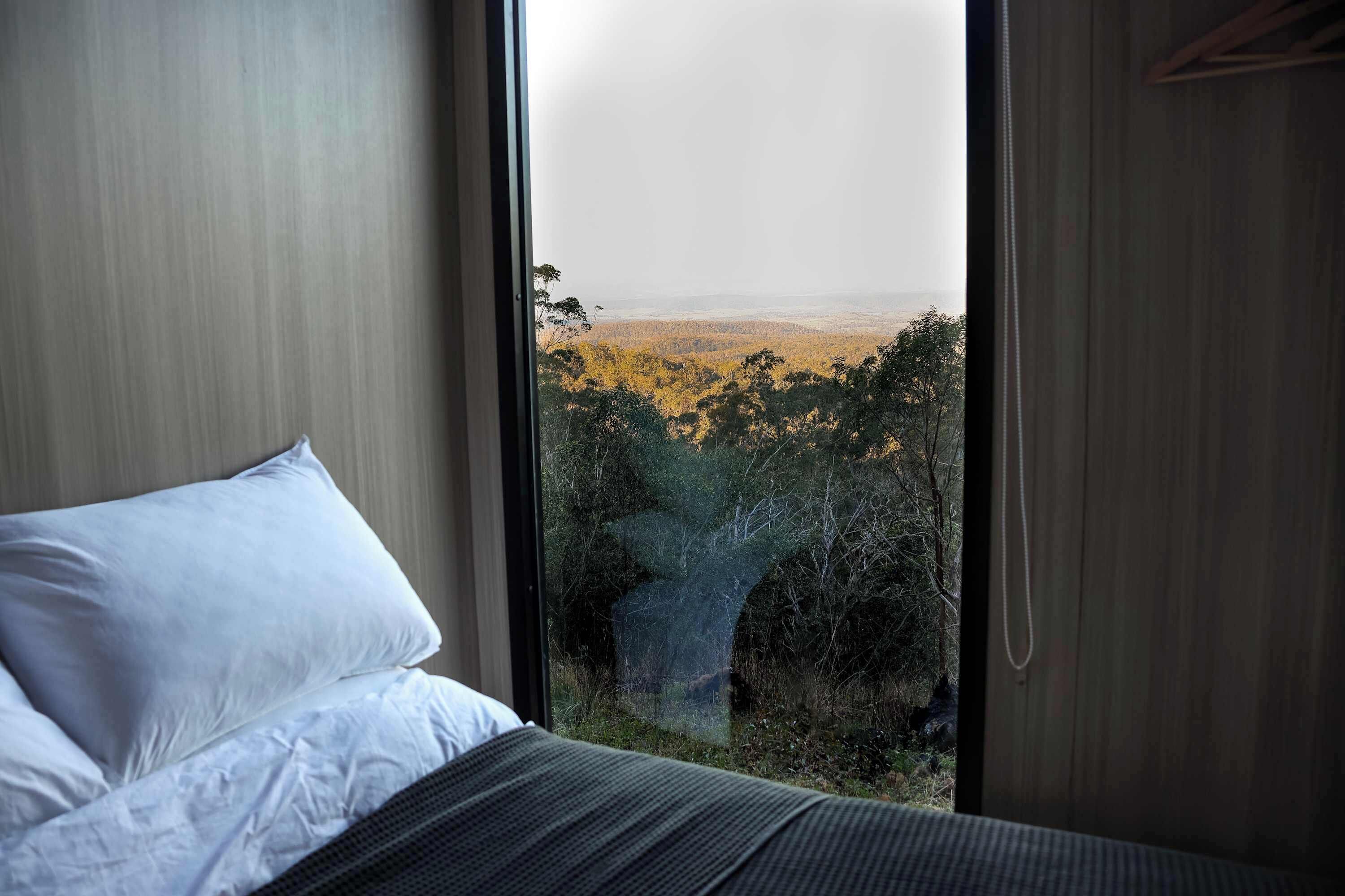 Un dormitorio con un ventanal que da a un paisaje boscoso.
