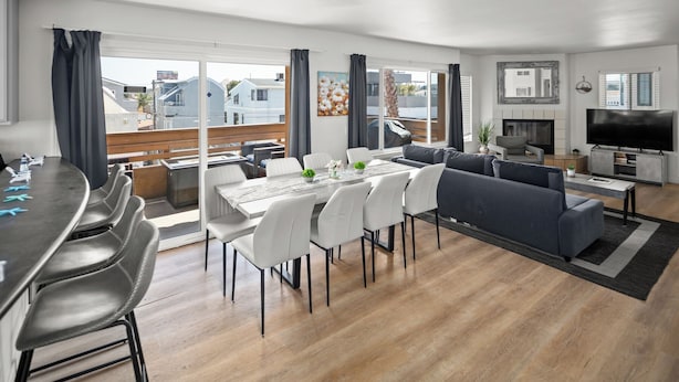 A modern living room with a dining area, a sofa set, a TV, and a fireplace. - Mission Beach 10BR · Steps to Bay & Ocean · Water Views · Firetable (San Diego)