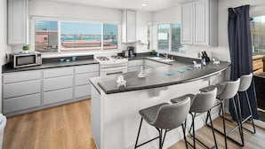 A modern kitchen with a central island, bar stools, and large windows. - Mission Beach 10BR · Steps to Bay & Ocean · Water Views · Firetable (San Diego)