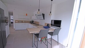 Eine moderne Küche mit weißen Schränken, einer Holz Arbeitsplatte und einem Essbereich mit zwei Stühlen.