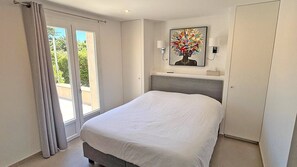 Ein Schlafzimmer mit Bett, einem Fenster mit Vorhängen, einem Bild an der Wand und einer Tür.