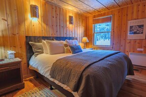 A wooden-paneled bedroom with a bed, bedside lamps, and a window.