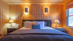 Una habitación con paneles de madera, una cama, dos lámparas de noche y un ventanal.
