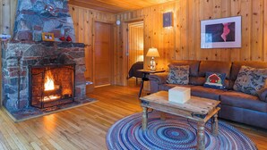 Una habitación acogedora con chimenea de piedra, paredes de madera, un sofá de cuero y un tapete redondo.