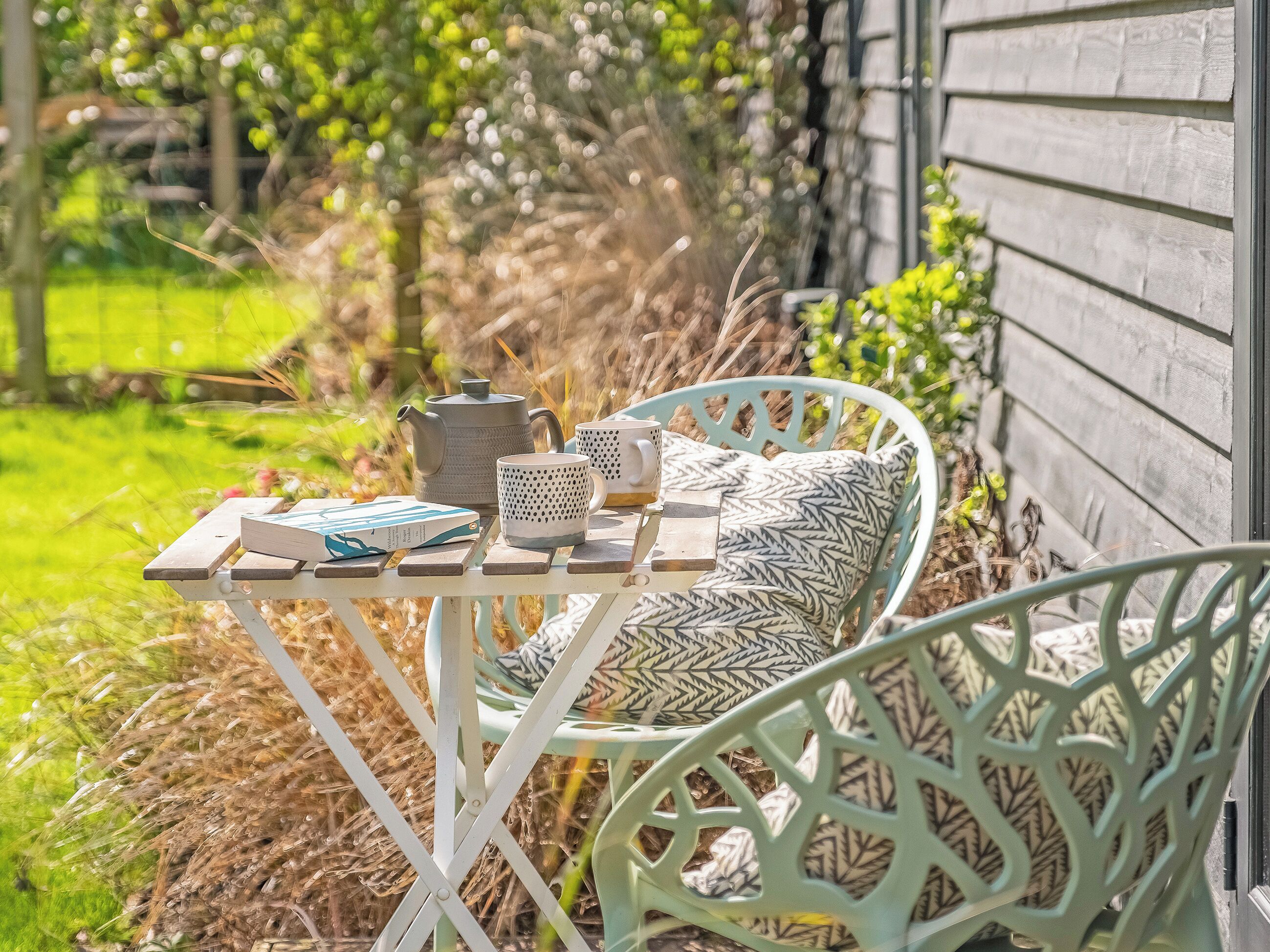 A metal table with a teapot, mug, and books on a bench outside a house.