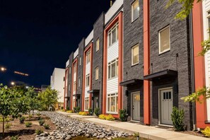 Une rangée de maisons de ville modernes à la façade en pierre, agrémentées de touches de couleur rouge et dotées d’un jardin paysager à l’avant, avec un petit élément décoratif aquatique.