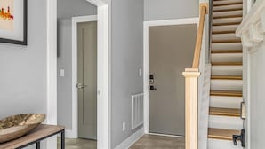 Un couloir avec un escalier, une porte et un luminaire fixé au mur.