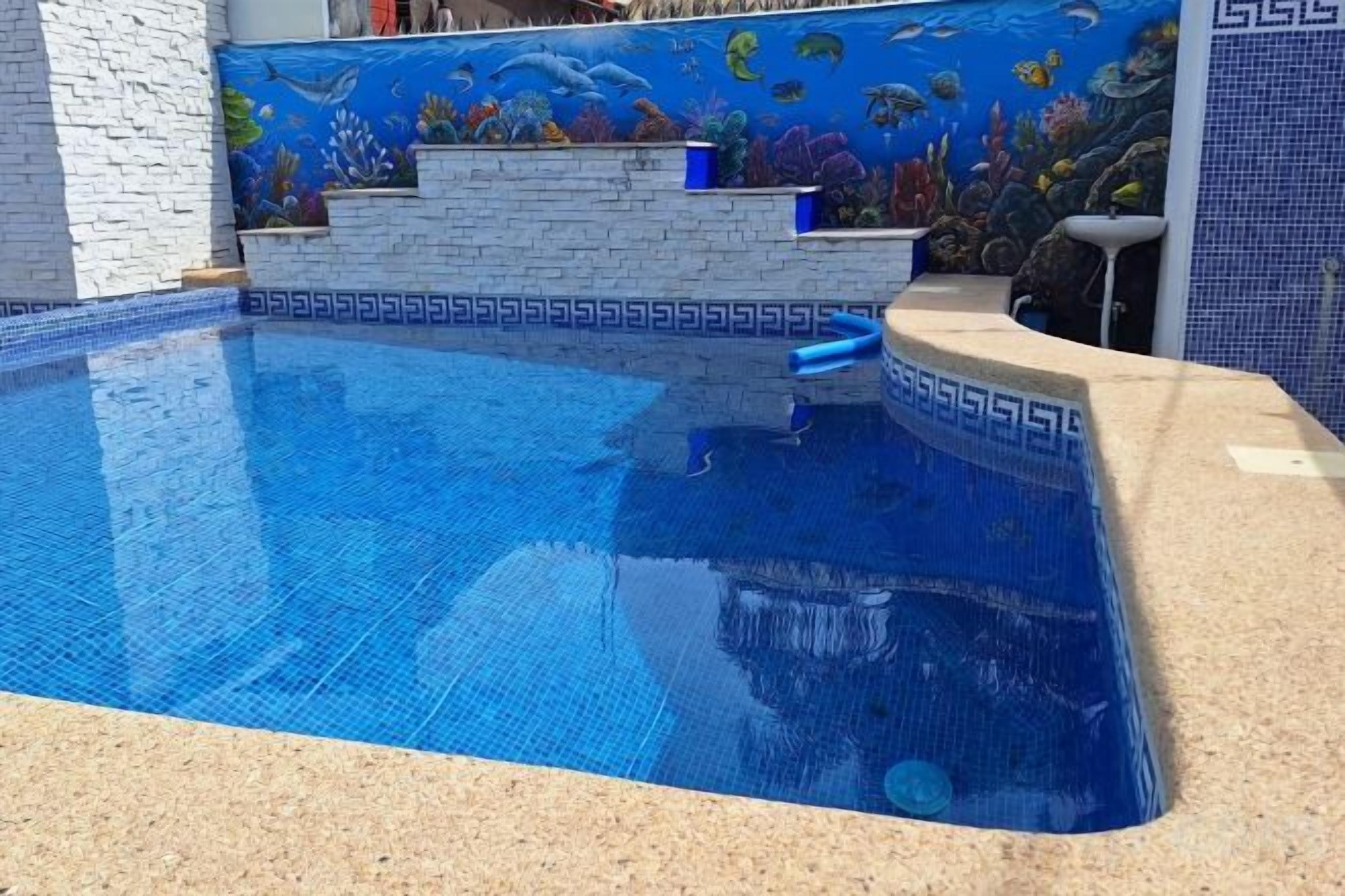 A swimming pool with a blue mosaic tile design, a stone ledge, and a wall mural.