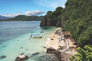 A coastal beach with clear turquoise water, rocky shore, and lush green cliffs. - La Casa Mariposa (Rincon de Guayabitos)