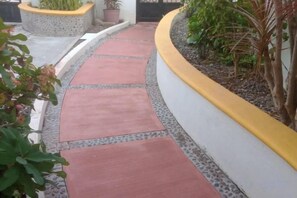 A curved pathway with red tiles leading to a white wall with a yellow trim. - La Casa Mariposa (Rincon de Guayabitos)
