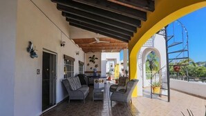 Eine überdachte Terrasse mit Gartenmöbeln, Fliesenboden und einem gelben Bogen.