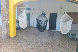 Un espacio de patio techado con hamacas colgantes, piso de baldosas y una puerta al fondo.