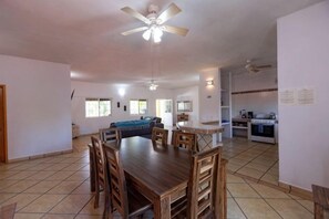 Un comedor amplio con una mesa y sillas de madera, un ventilador de techo y una cocina al fondo.