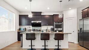 Una cucina moderna con mobili scuri, elettrodomestici in acciaio inossidabile, un'isola centrale con sgabelli da bar e illuminazione a sospensione.