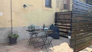 Une terrasse extérieure avec une table et des chaises, une plante en pot et une clôture en bois.
