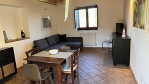 Un coin repas avec une table et des chaises, un canapé, un radiateur, une fenêtre et un téléviseur posé sur un meuble.