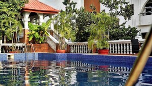 A swimming pool with a tiled edge, surrounded by potted plants and a white balustrade.