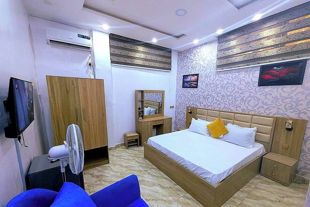 Una habitación de hotel con cama, escritorio, silla, armario, espejo y televisor.