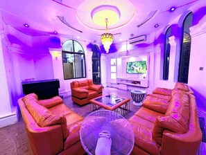 A room with leather sofas, a glass coffee table, a large fan, and a TV. - Frenezia Boutique Apart-Hotel (Lagos)