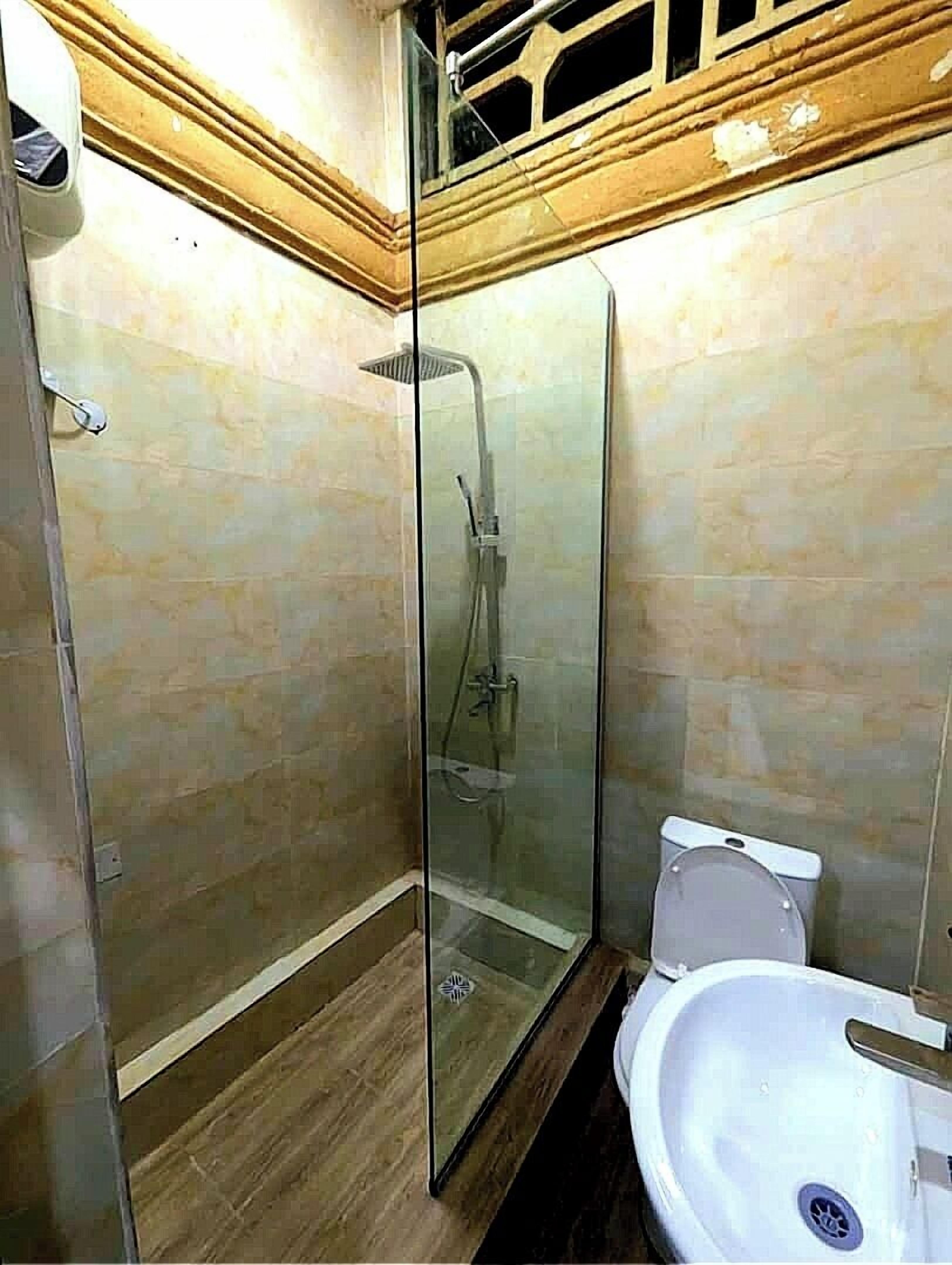 A glass-enclosed shower with a handheld showerhead, a white sink, and a toilet.