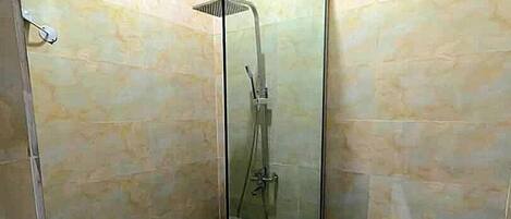 Una ducha con cerramiento de vidrio, un cabezal de ducha manual, un lavamanos blanco y un inodoro.