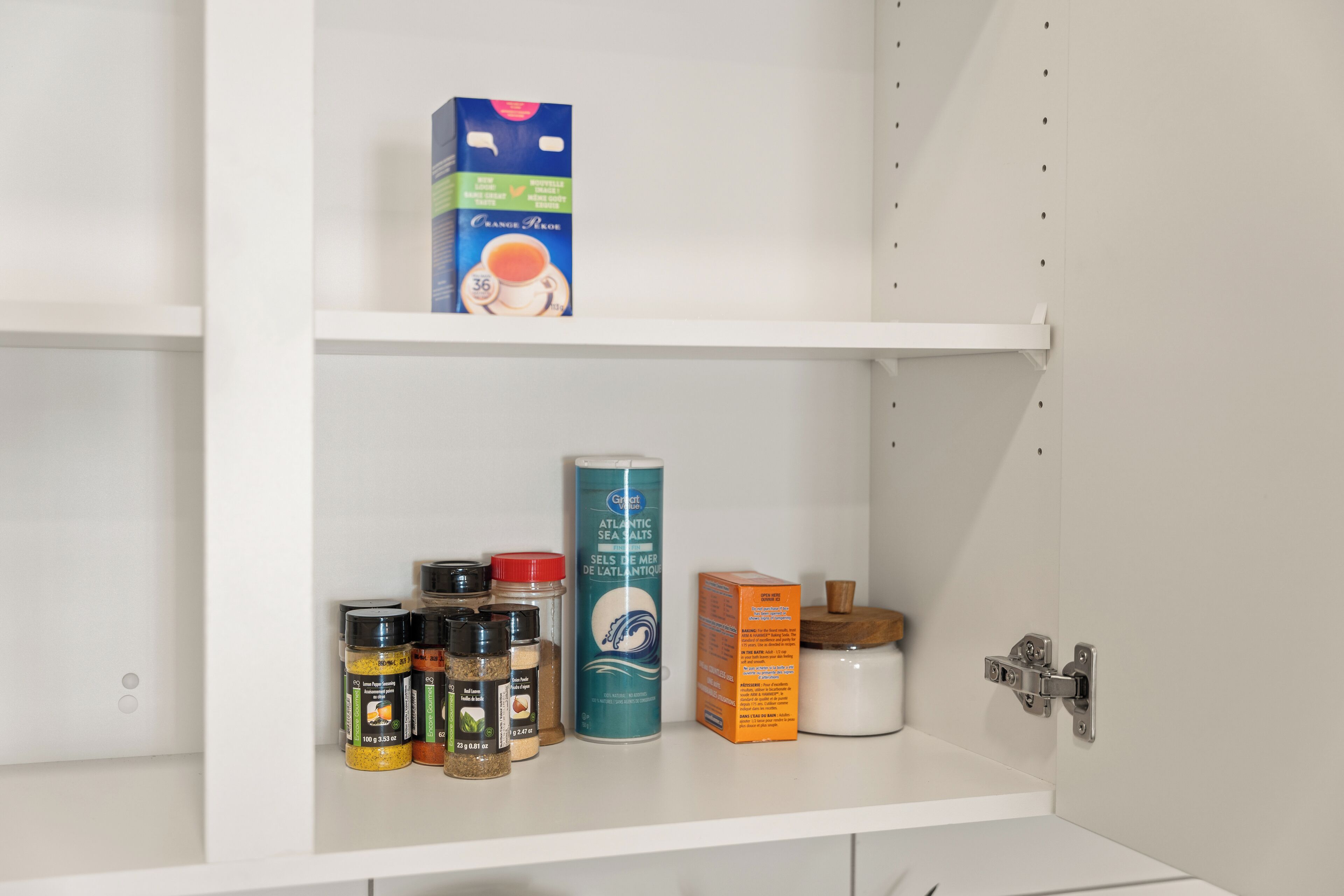 Un estante blanco con varios artículos de cocina, entre ellos especias, un bote de Sal Marina Atlántica y una caja de crema para café.