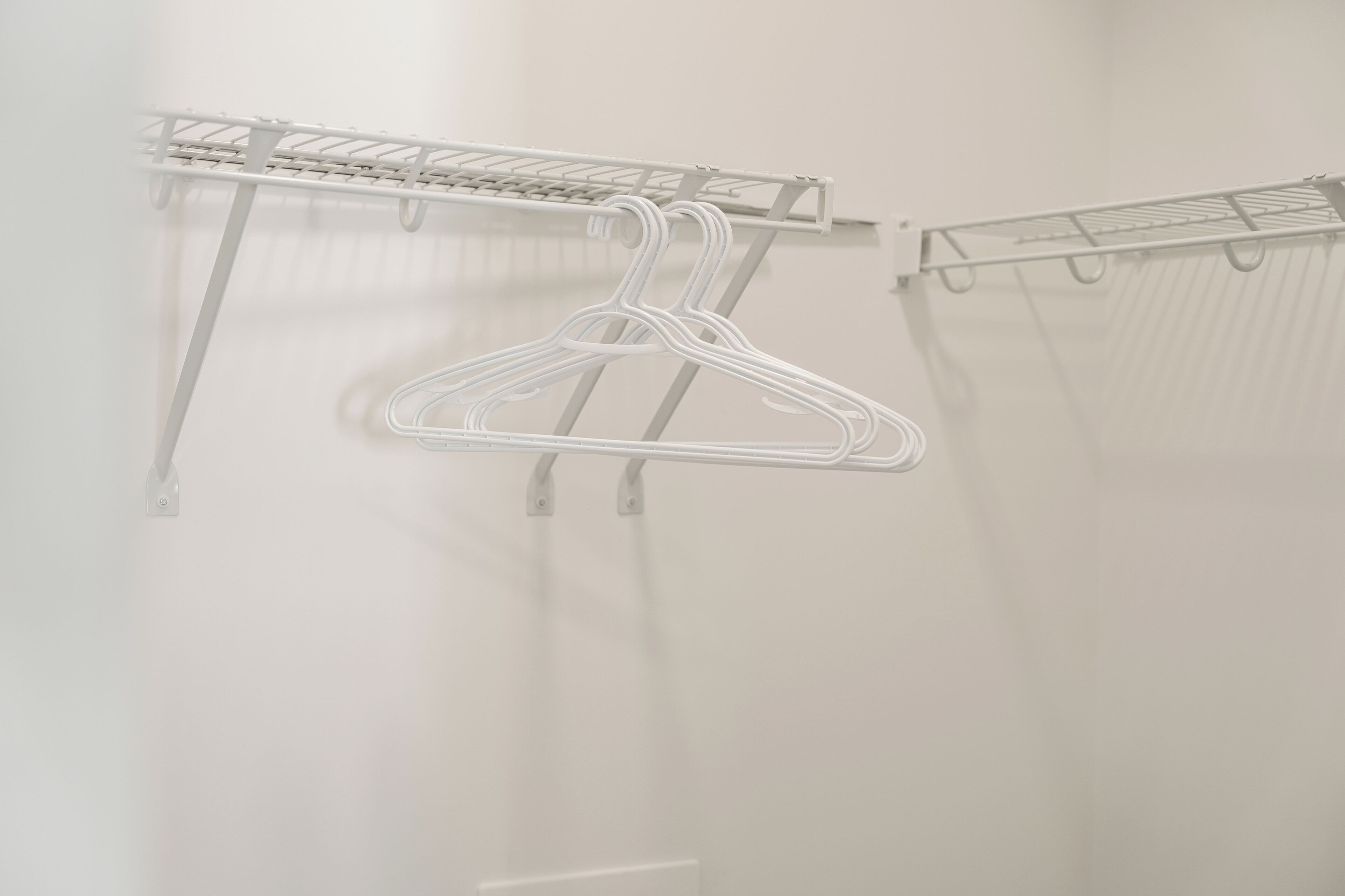 A white metal drying rack with multiple hangers against a plain wall.