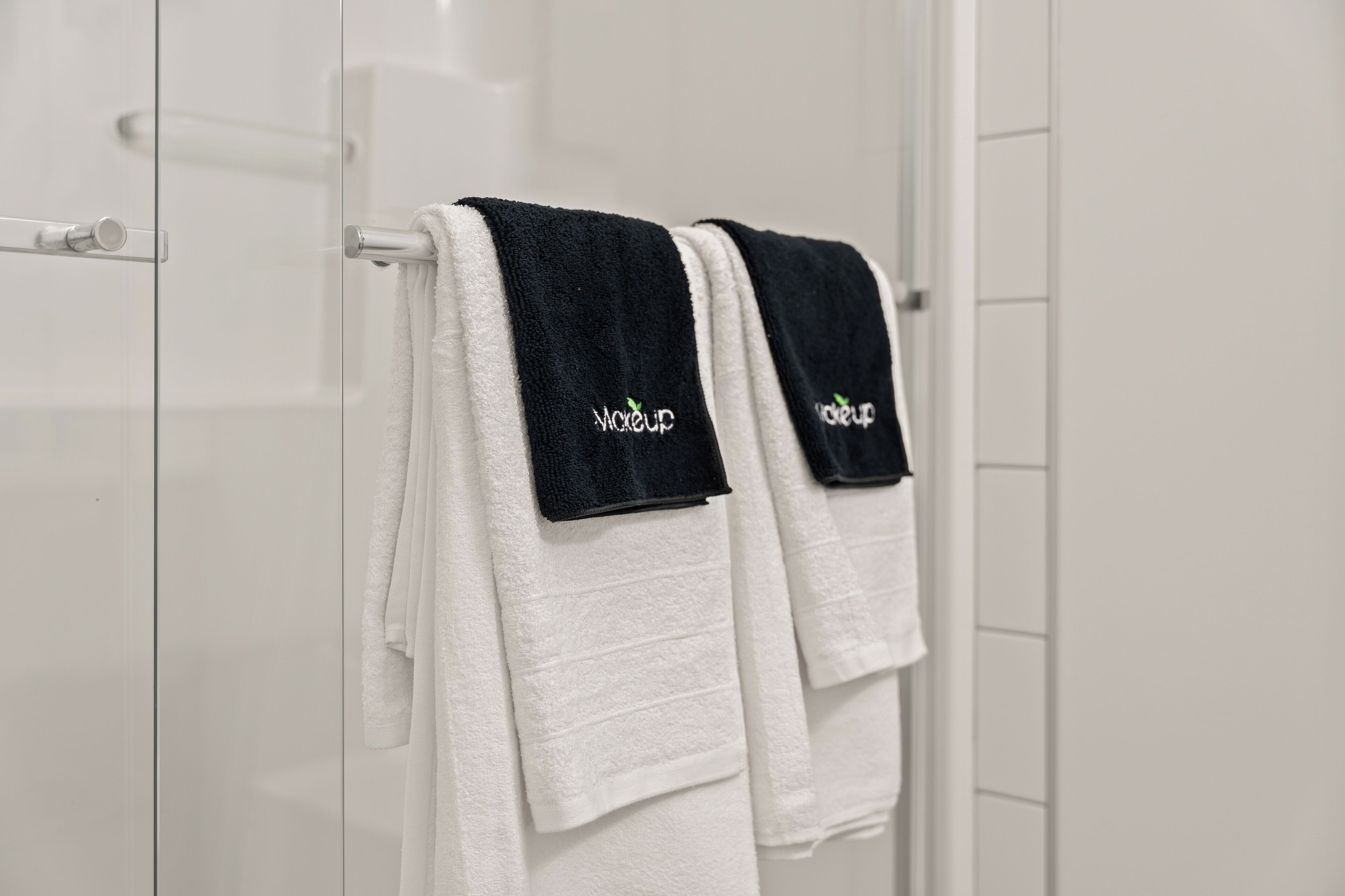 Twee witte handdoeken met zwarte labels hangen aan een witte handdoekhouder in een badkamer.
