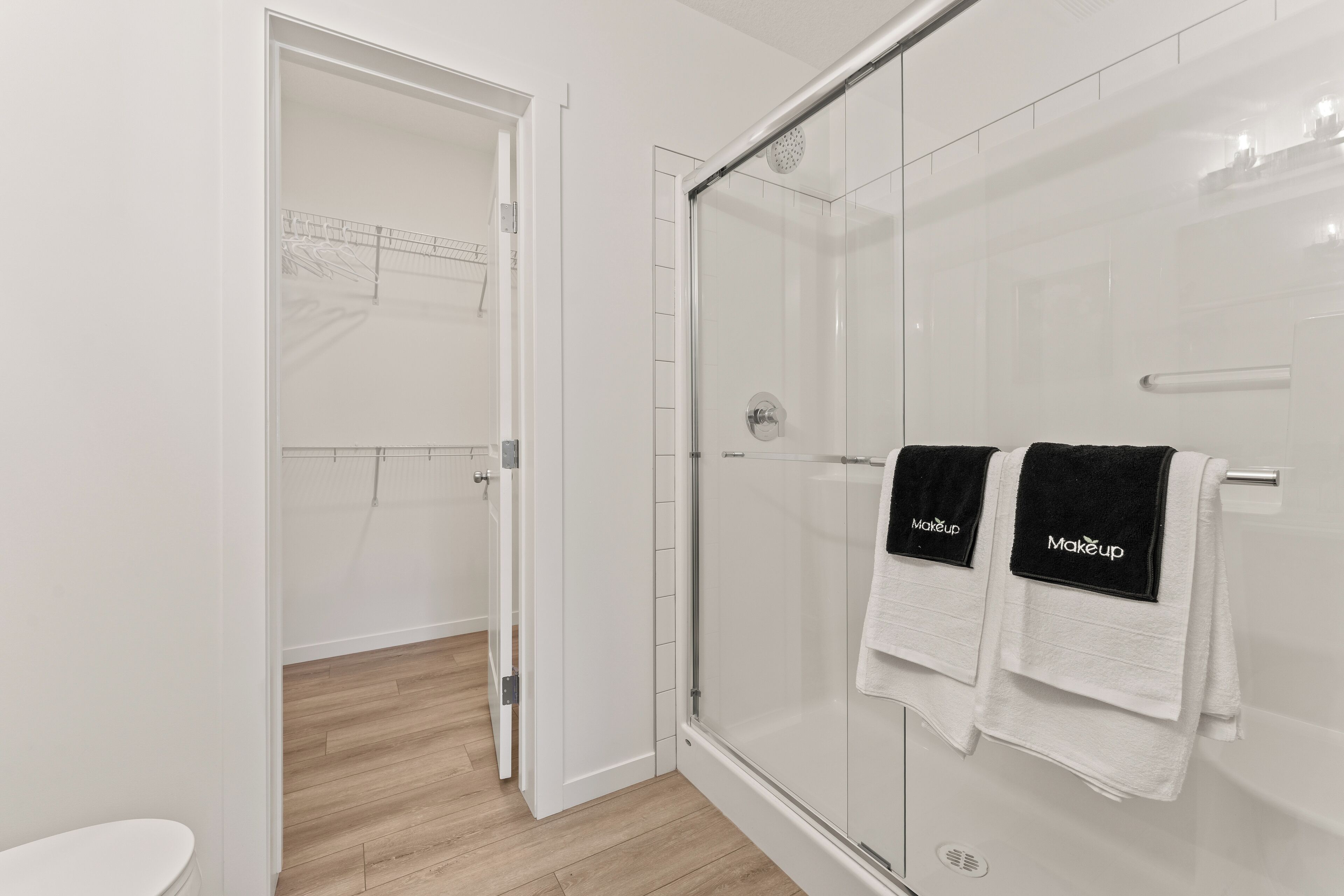Un baño moderno con cabina de ducha de vidrio, un inodoro blanco y dos toallas con la marca 'Makeup'.