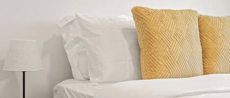 A neatly made bed with white and textured pillows, a lamp on a bedside table, and a remote control.