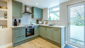 A modern kitchen with light green cabinets, a built-in oven, and a window with a view of trees. - 2 bedroom accommodation in Torquay (Torquay)