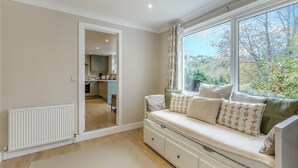 A room with a built-in bench with storage drawers, a large window with a view of trees, and a kitchen in the background. - 2 bedroom accommodation in Torquay (Torquay)