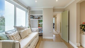 A modern living room with a sofa, a bookshelf, and a view through a large window. - 2 bedroom accommodation in Torquay (Torquay)