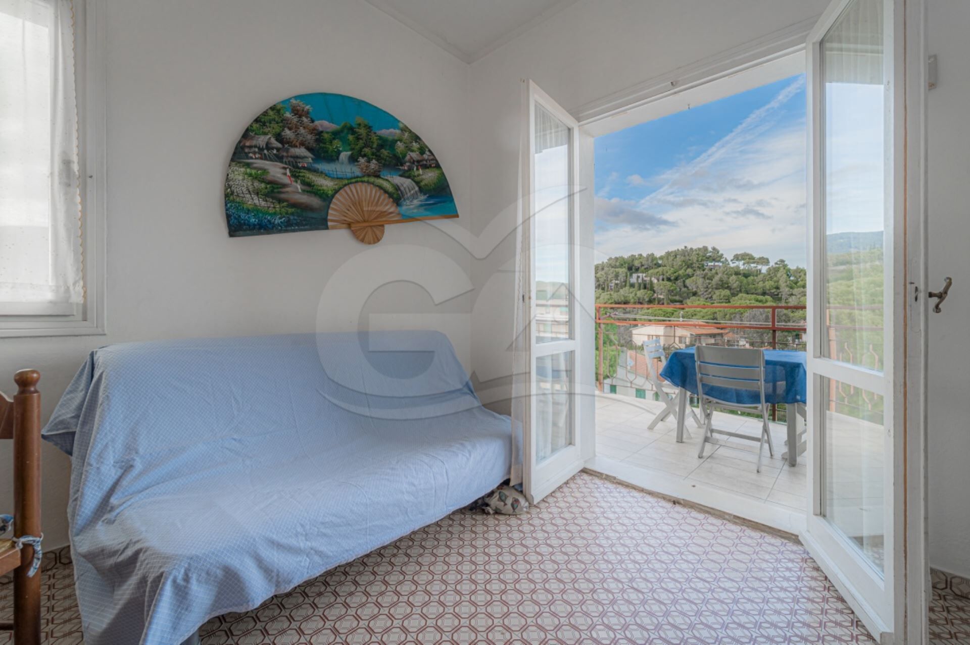 A bedroom with a bed, a painting, and a balcony with a table and chairs.