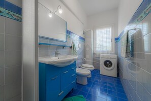 Ein Badezimmer mit Waschbecken, zwei Toiletten, einer Waschmaschine und einem Fenster mit Vorhängen.