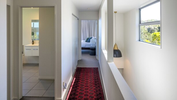 A hallway with a red patterned carpet, a bed with white curtains, and a window with a view of greenery. - Bellevue, Onetangi - Sea Views, Modern Comfort, and Relaxation (Waiheke Island)