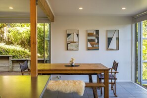 A dining area with a wooden table, chairs, and a bench. There are three artworks on the wall.