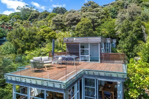 A modern house with a wooden deck, glass-enclosed patio, and a view of lush greenery.