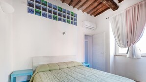 Een slaapkamer met een bed, een blauwe nachtkastje, een wit hoofdeinde, een wandairconditioner, een deur en een raam met gordijnen.
