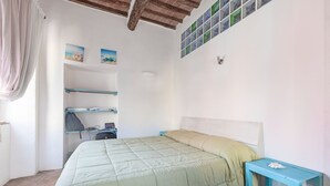 A bedroom with a bed, a nightstand, a shelf unit, and a wall with pictures.
