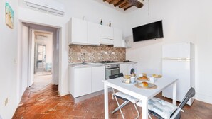 A compact kitchen with white cabinets, a tiled backsplash, a built-in oven, and a dining table with breakfast items.