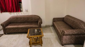 Una sala de estar con dos sofás estampados, una mesita de madera y una cortina roja.