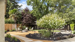 A backyard with a patio area, outdoor furniture, a tree with white flowers, and a wooden fence. - Hawaiian Coffee Hale (Redding)