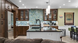 A modern kitchen with wooden cabinets, a large island, and a backsplash of blue and green tiles. - Hawaiian Coffee Hale (Redding)