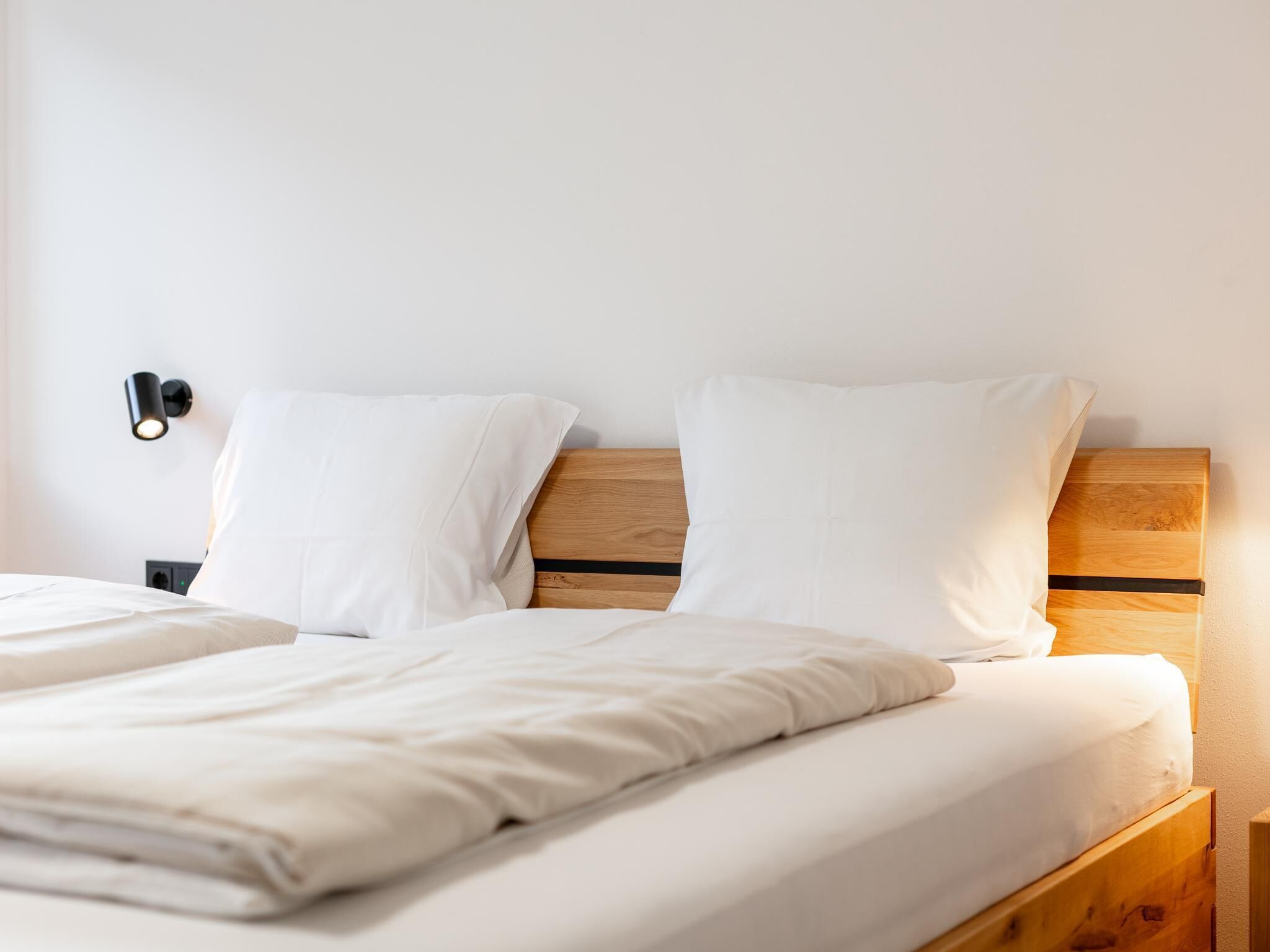 A neatly made bed with white bedding, a wooden headboard, and a nightstand with a lamp.